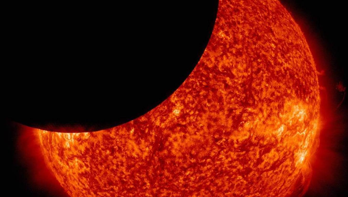 A telescope view of a partial solar eclipse, with the black shadow of the Moon crossing the fiery red disc of the Sun