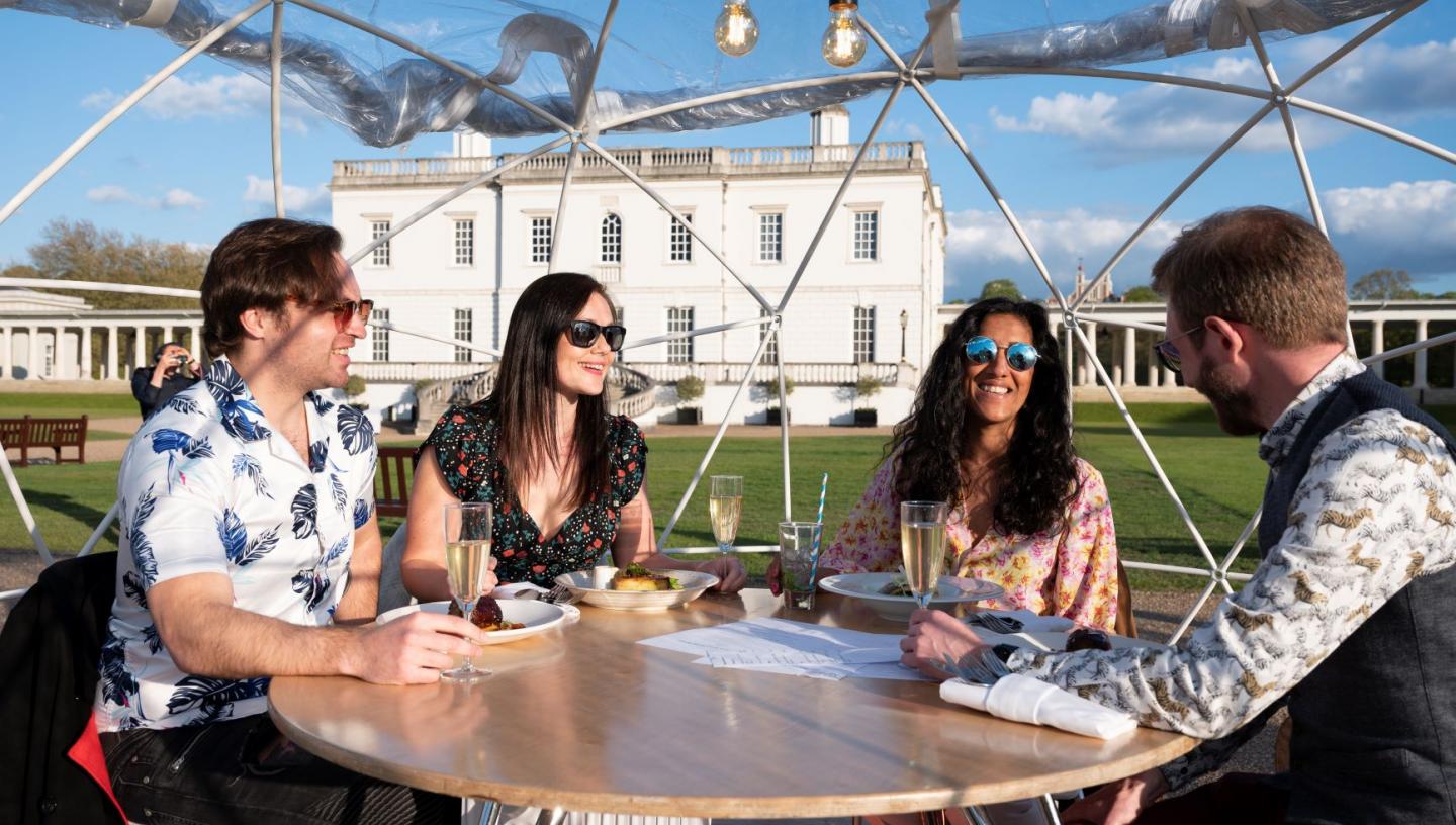 A group dining in a pod inside the Queen's House Dining Domes, with the House in the background