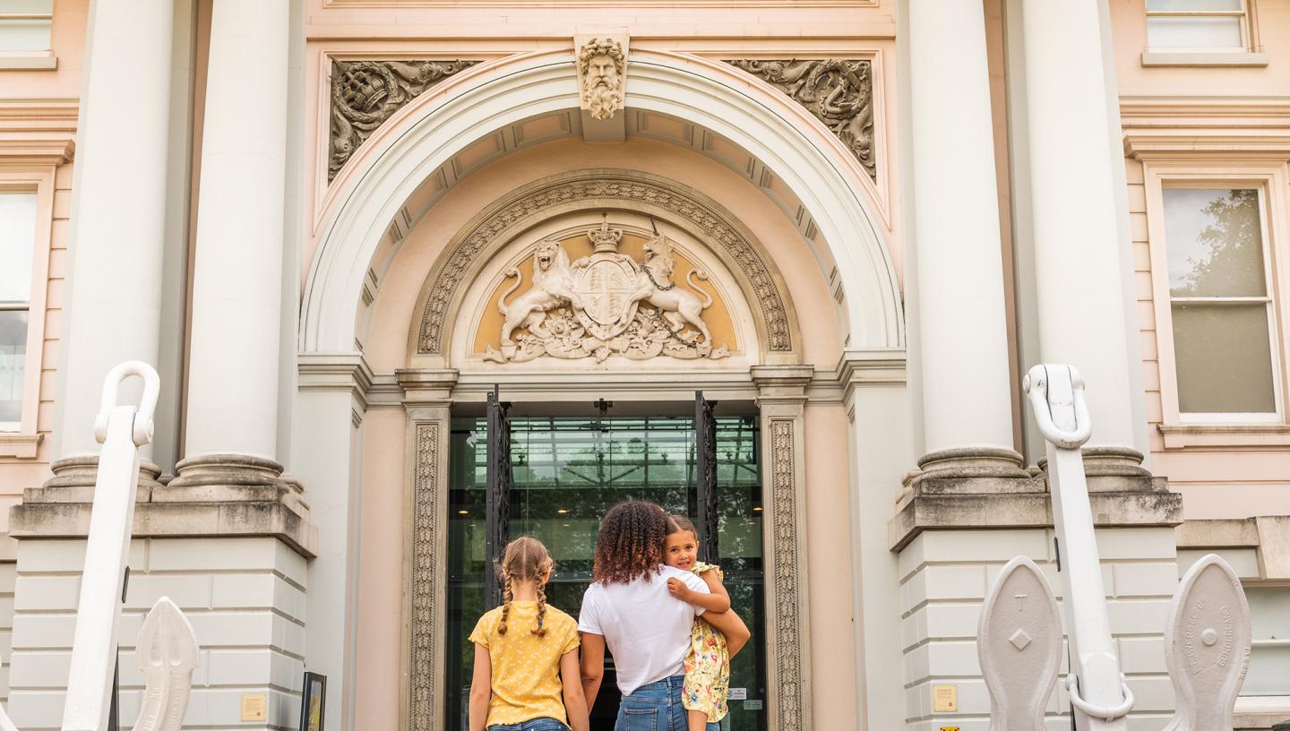 A family walks through the main entrance of the National Maritime Museum in Greenwich, London