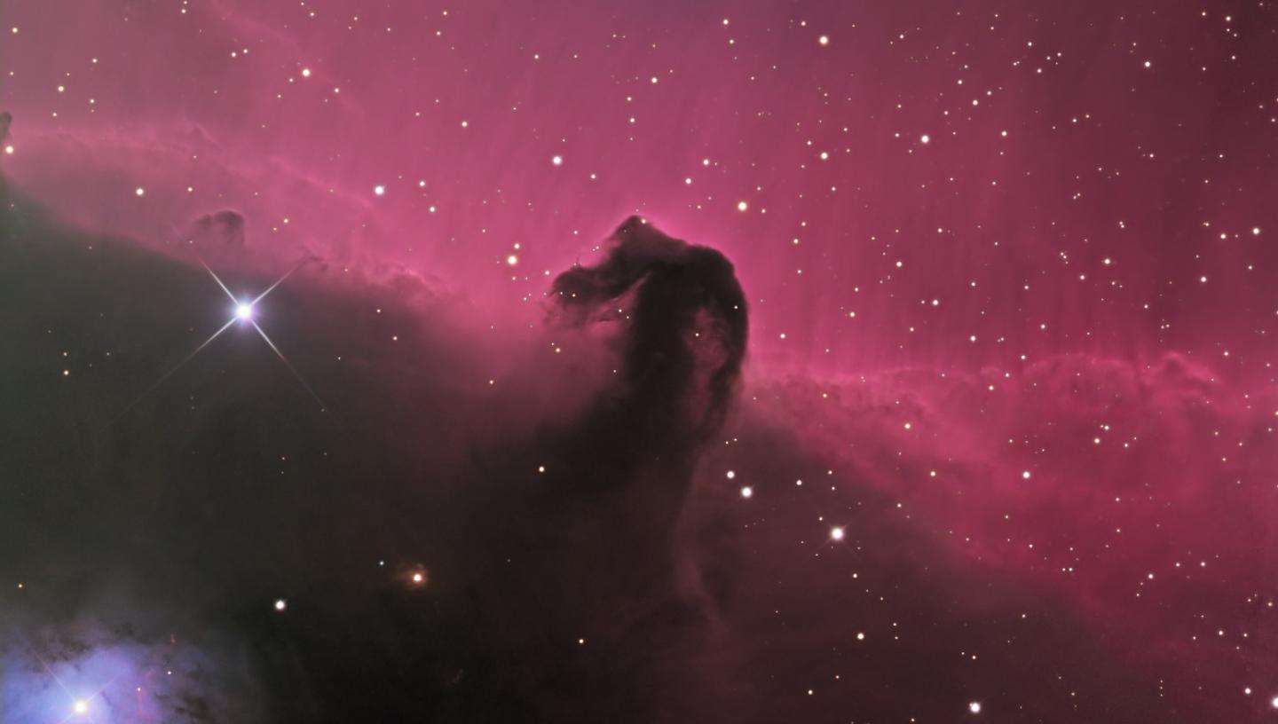 A deep space astrophotograph of the horesehead nebula, with pink curtains of light and bright blue-white pinpricks of stars