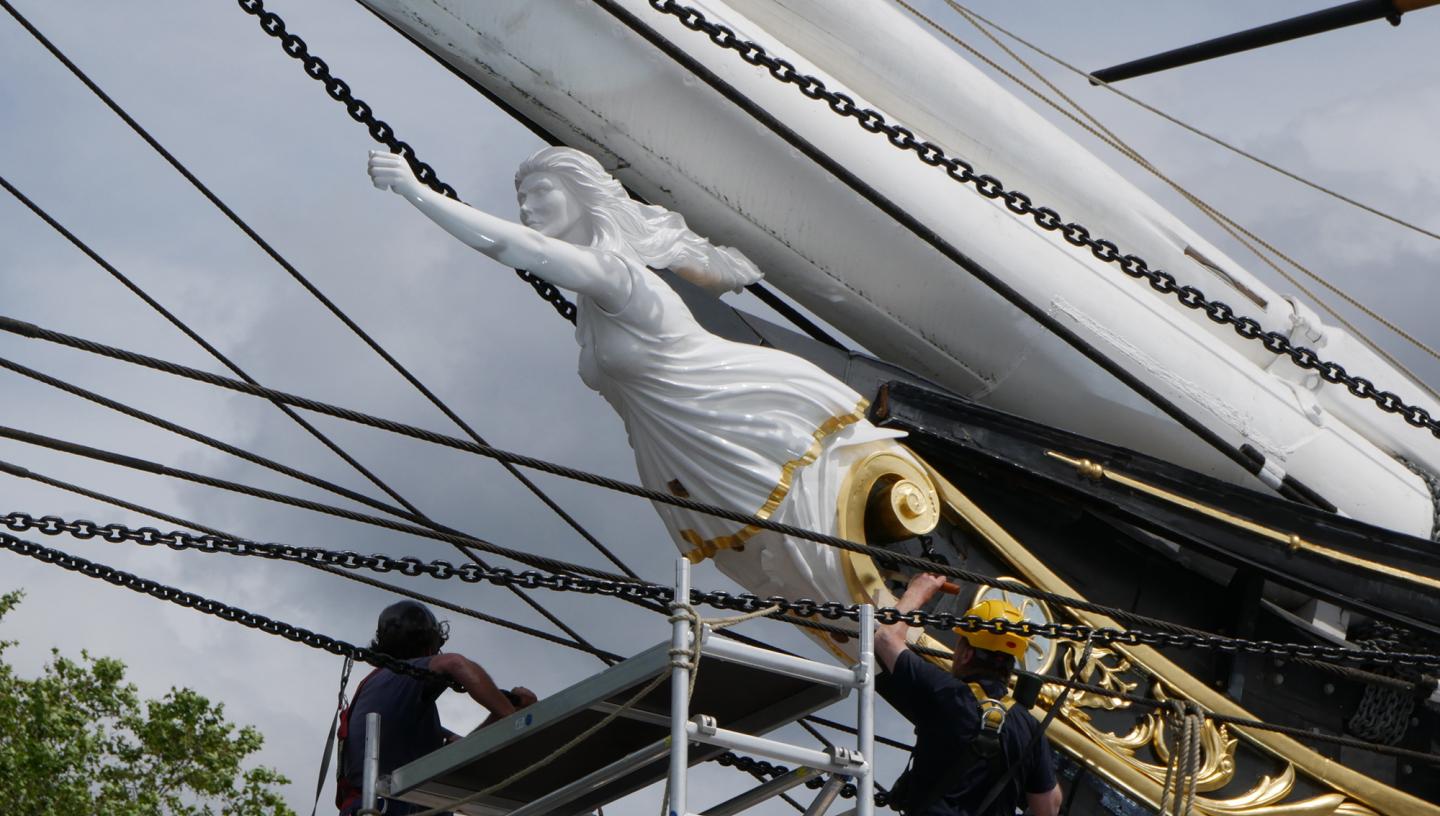 The new figurehead for historic ship Cutty Sark during installation. Workers standing on scaffolding fix the sculpture in place