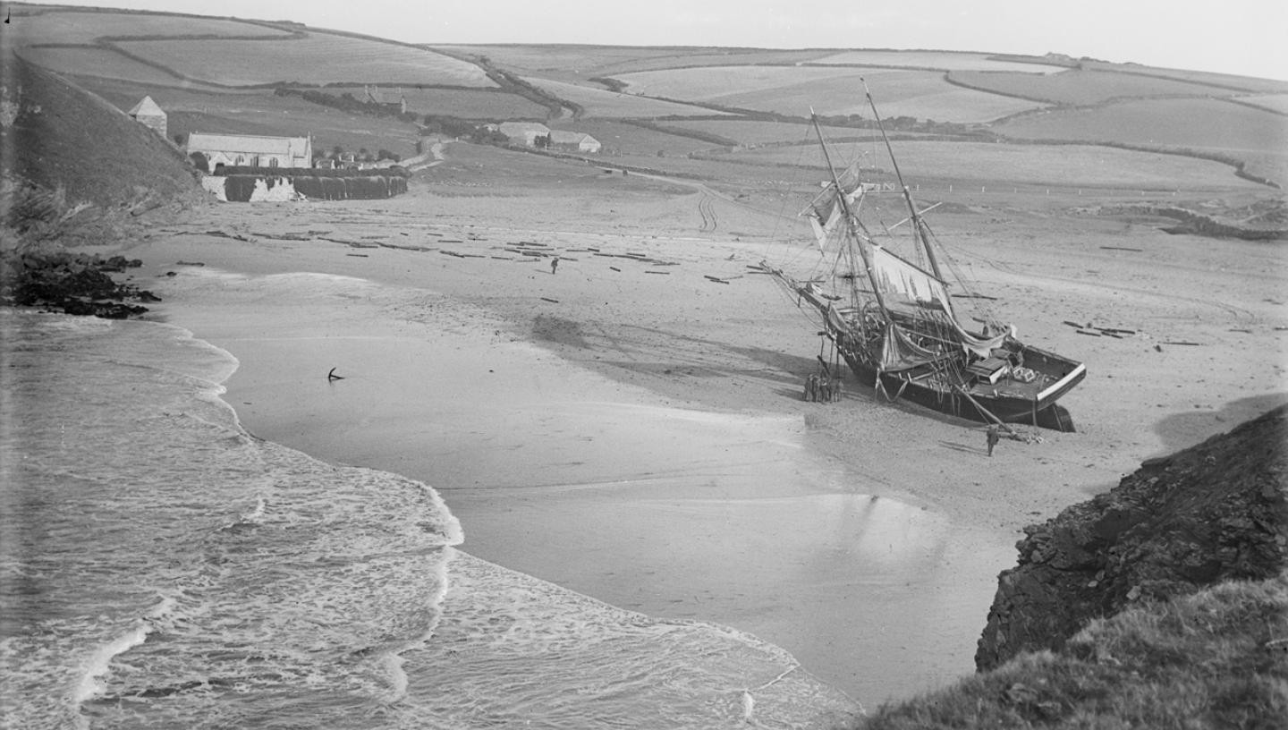 HIstoric black and white photograph of a sailing ship stranded on a beach