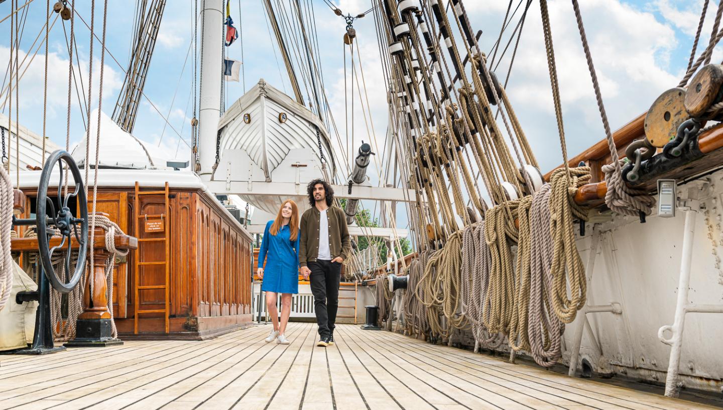 A man and a woman walk hand in hand along the main deck of historic ship Cutty Sark