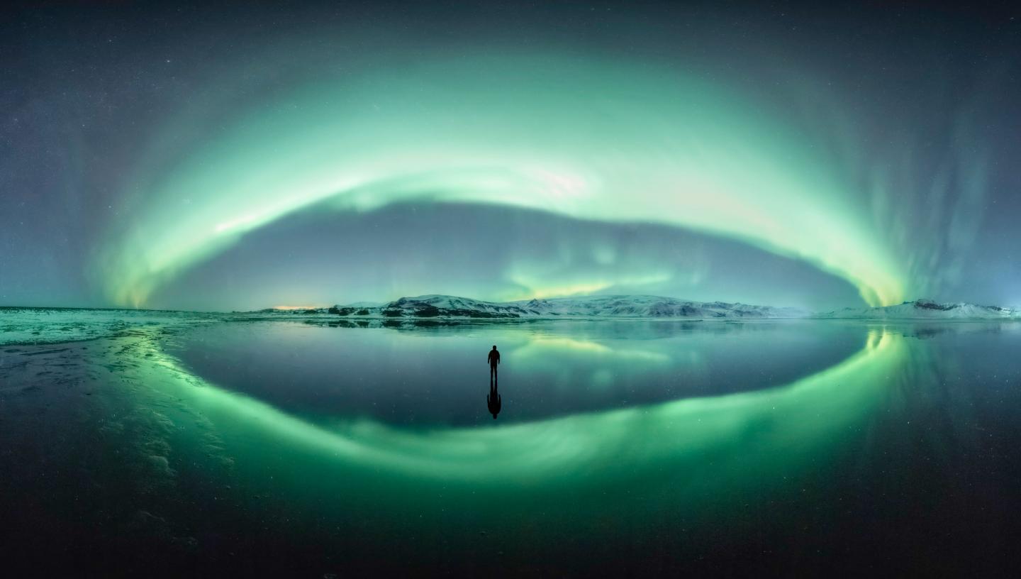 A man stands looking at green bands of aurorae in Iceland