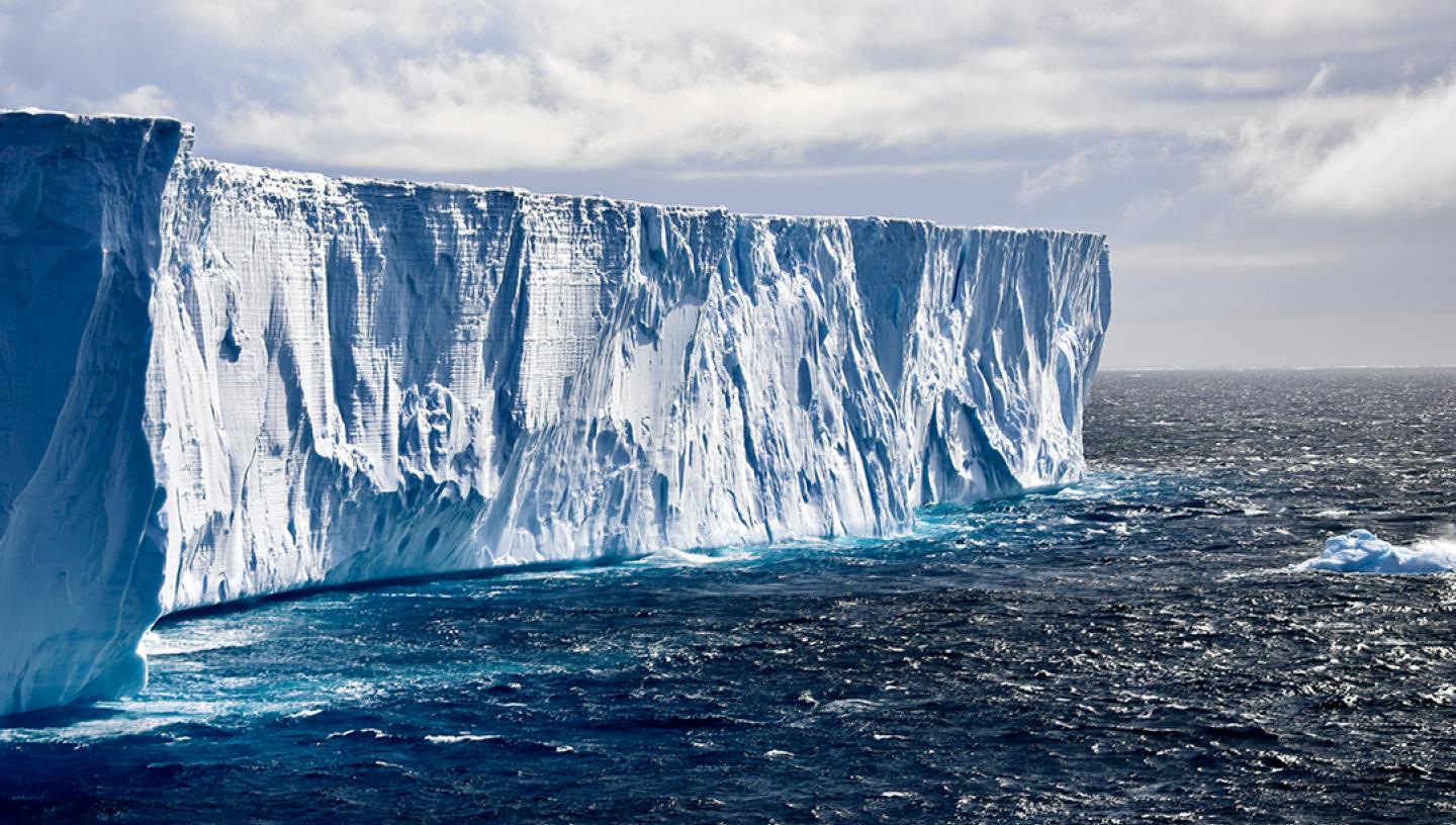 The face of an iceberg falls away to a dark blue ocean