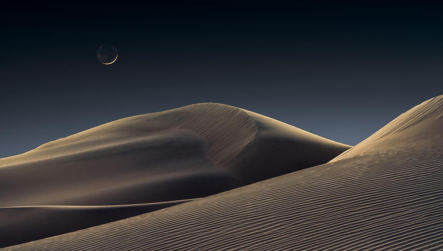 Crescent Moon rising above sand dunes