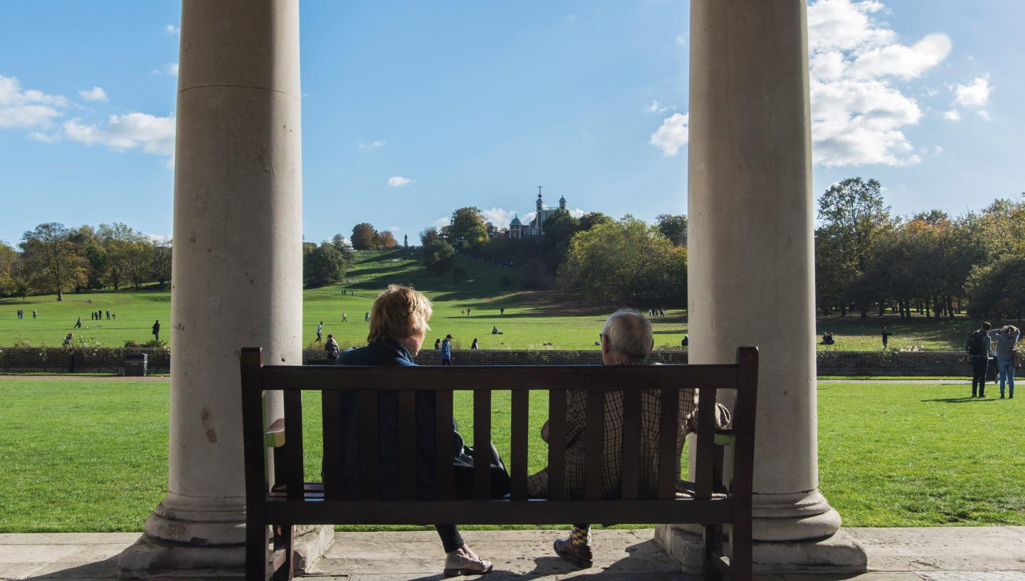 Two people chatting on a bench with a view Greenwich park and the Royal Observatory Greenwich 