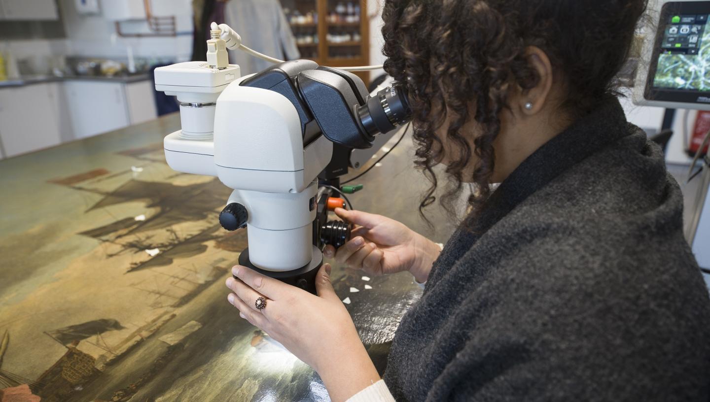 A woman analyses an oil painting using a microscope as part of the painting's conservation process