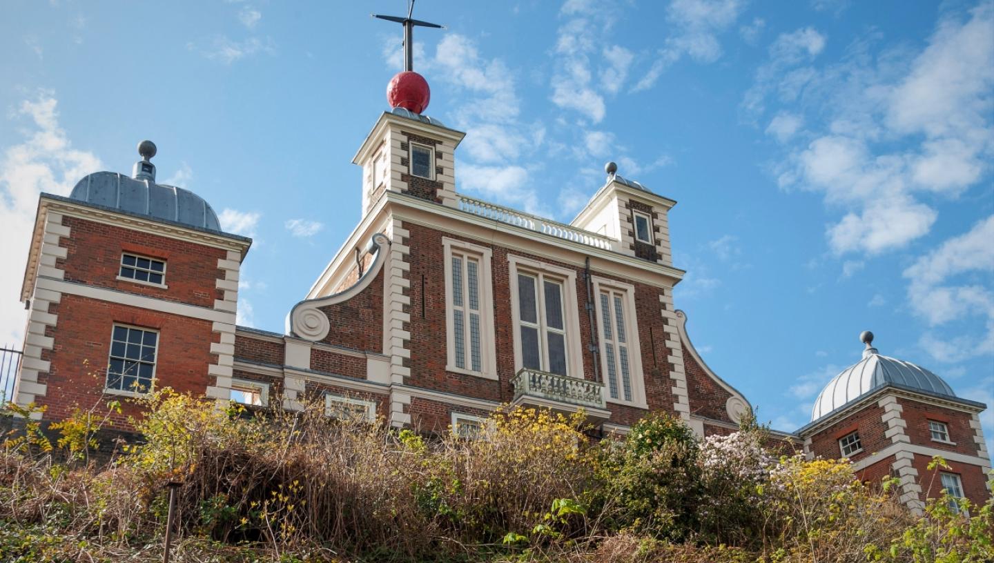 View of the Royal Observatory Greenwich from below. The brick facade of Flamsteed House and the red Time Ball on the roof are visible