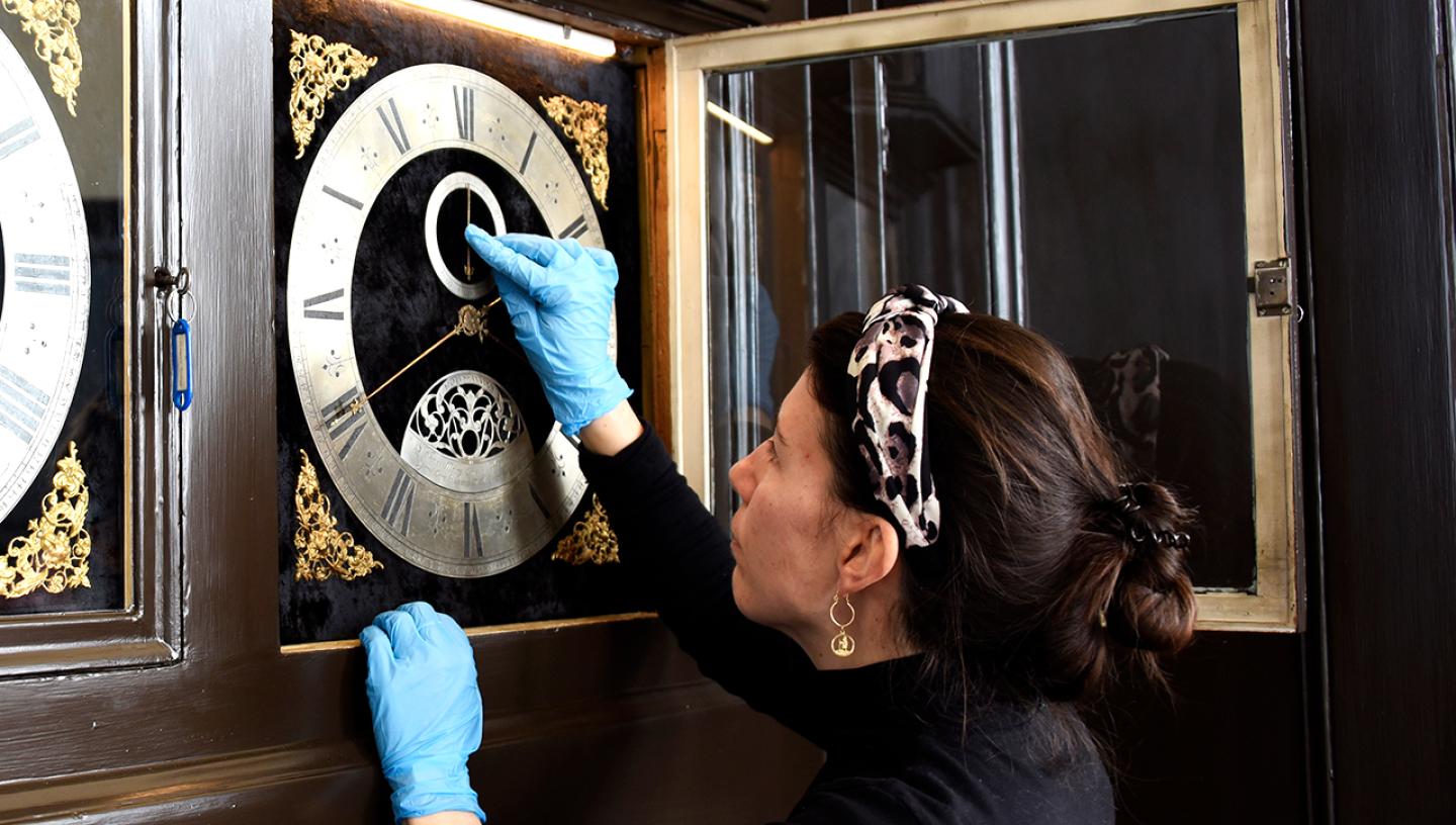 A woman wearing blue surgical gloves examines a historic clock during conservation work in the Royal Observatory's Octagon Room