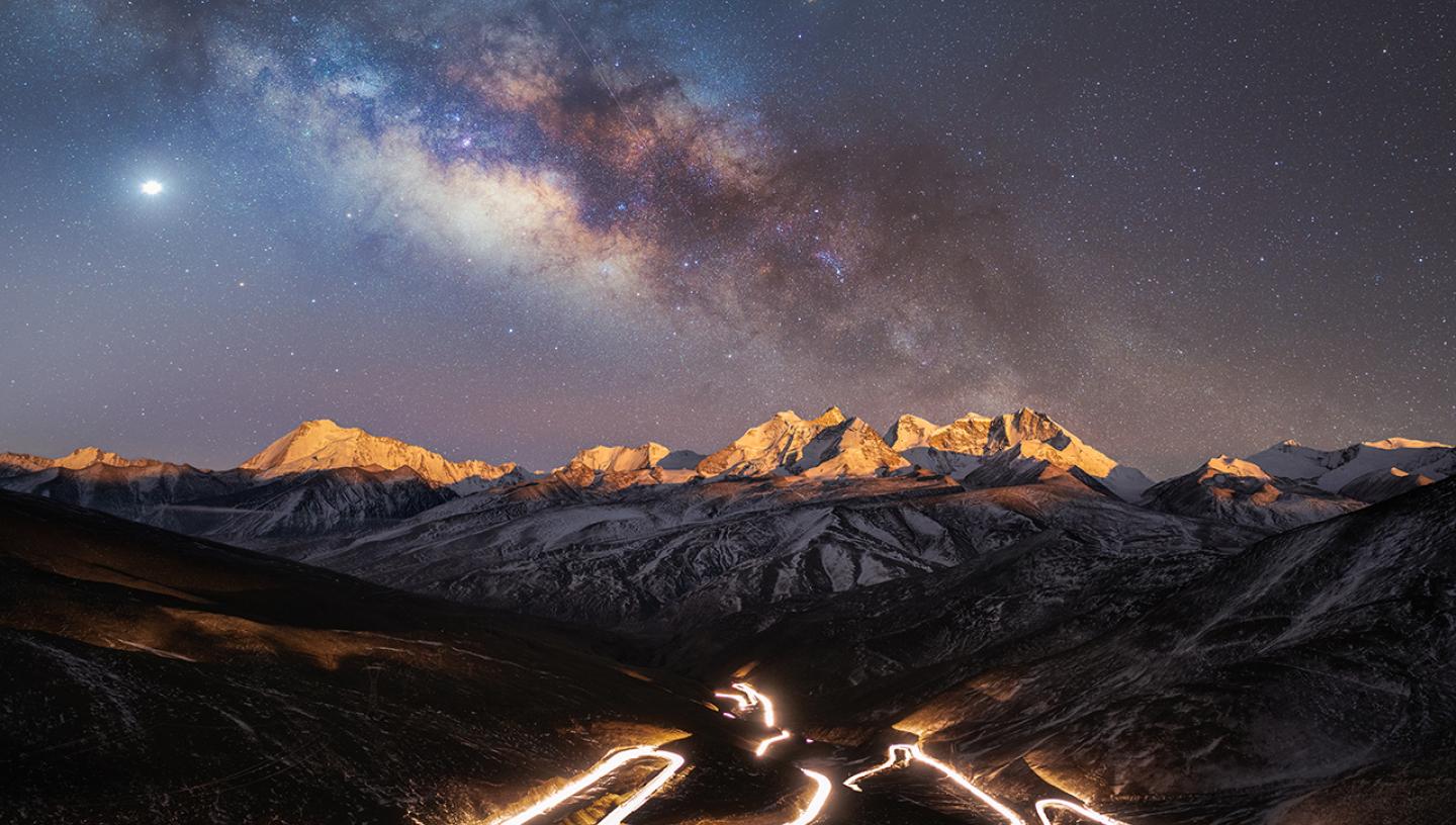 Long exposure of a long highway on a mountain with mountains and starry sky in the background