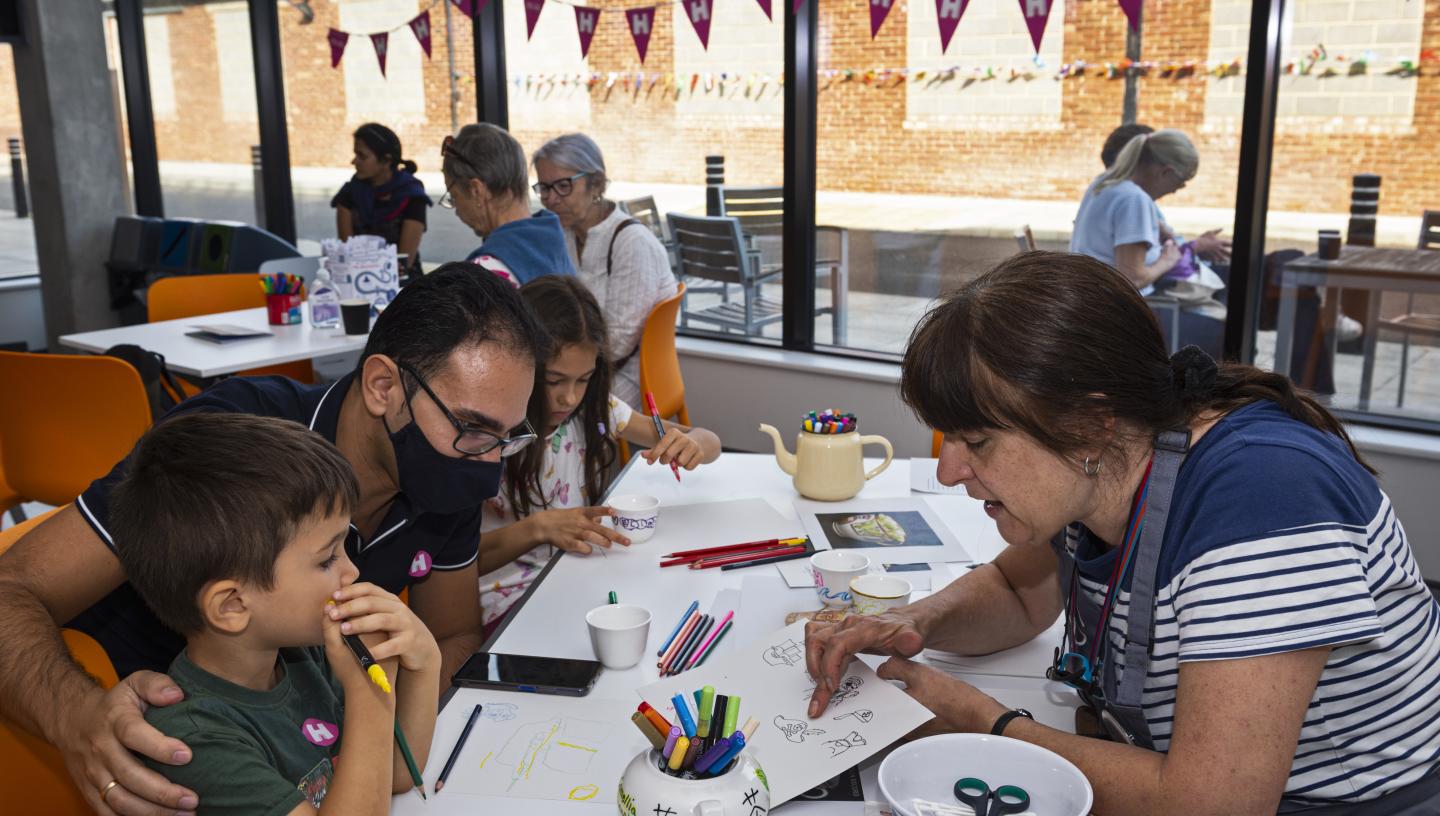 Family enjoying Heritage Open day in a big room with white tables and large windows, they are doing a craft activity