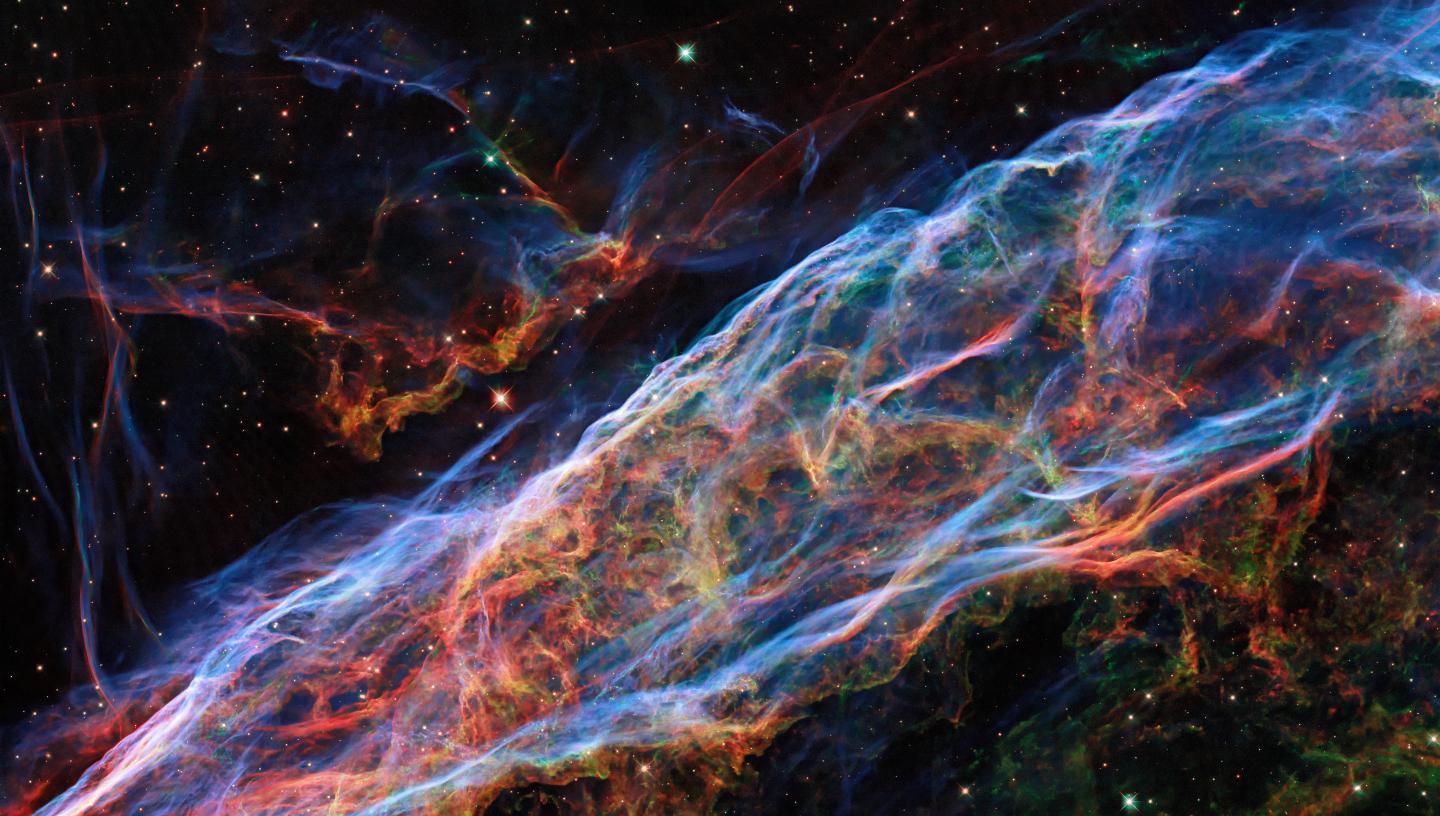 The Veil Nebula as seen by the Hubble Space Telescope. Filaments of blue, green, and red light cover the image, tracing different gases inside the curtain-like cloud.