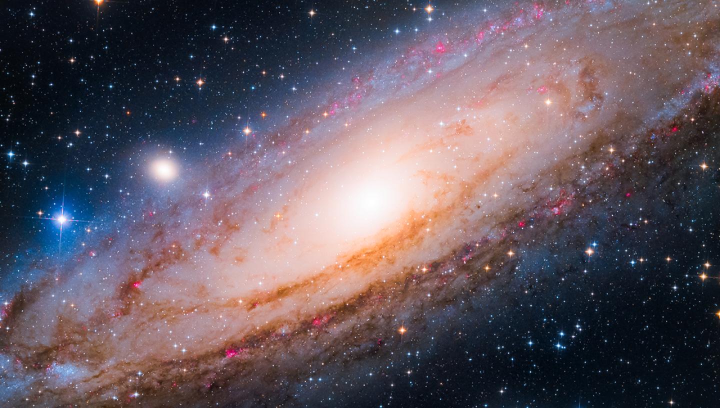 Astrophotograph of the Andromeda Galaxy, showing a spiral of stars tinted from bluey-pink to white at the centre