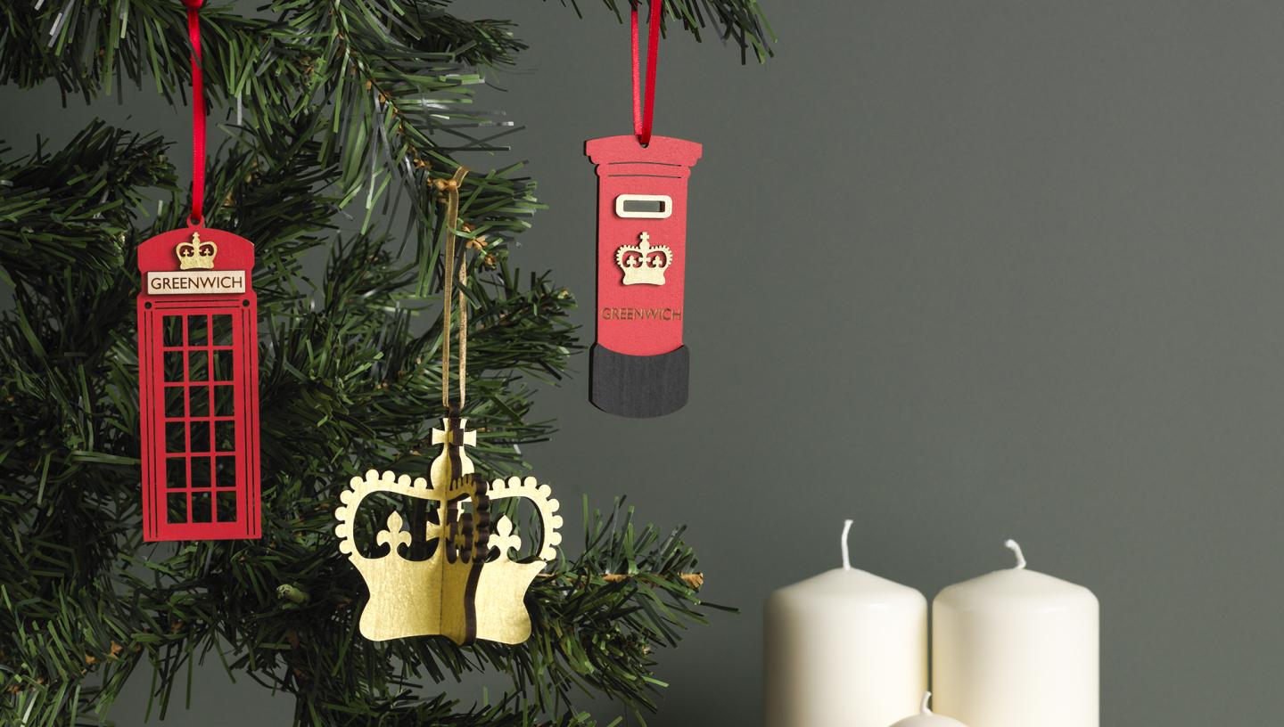 Christmas decorations in the shape of a crown, a phone box and post box hang from a Christmas tree, with three chunky candles displayed beneath