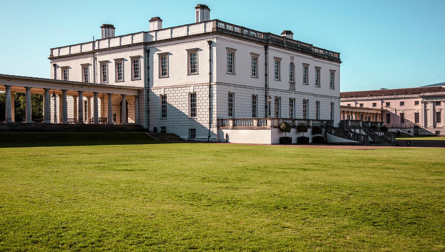 A view of the Queen's House in Greenwich from the outside. The square white building is seen from an angle, with green grass stretching up to the main entrance