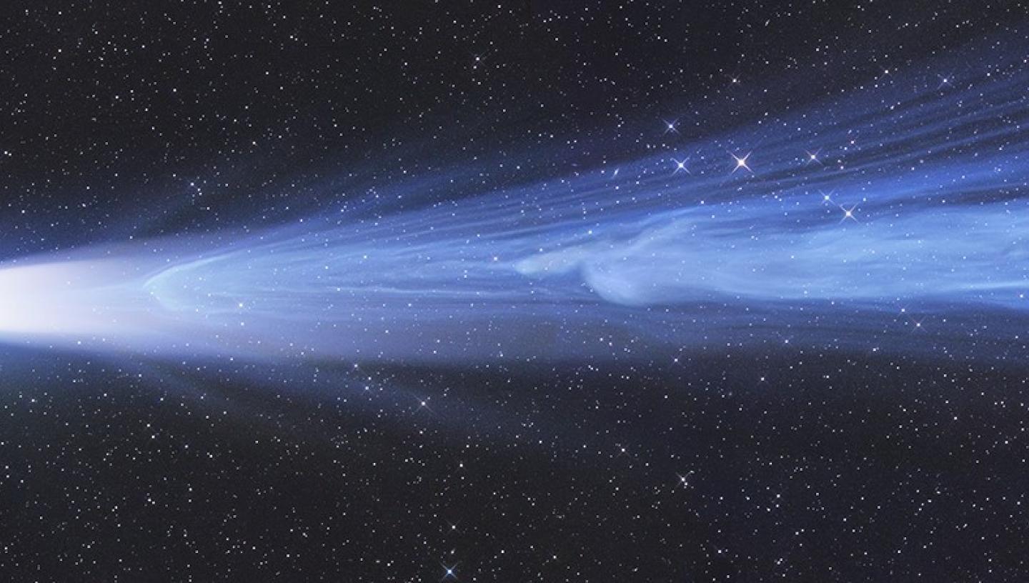 Long letterbox shaped image of a long blue comet with a green head, in the right hand side of the image there is a piece of the comet's tail coming off of the rest