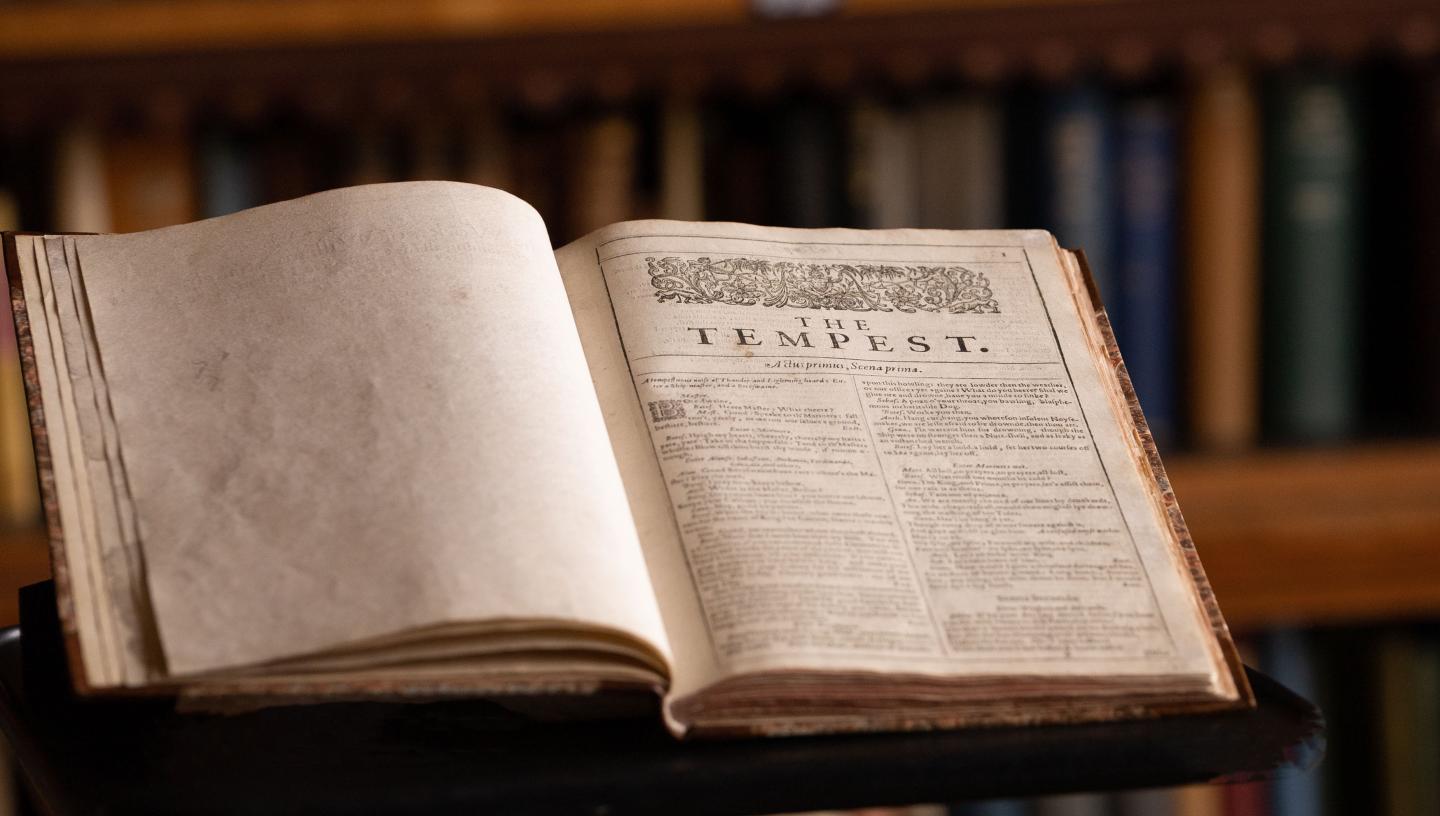 A photograph showing a page from Shakespeare's First Folio owned by Dulwich College. The edition is laid open at the first page of The Tempest, with shelves of books just visible in the background