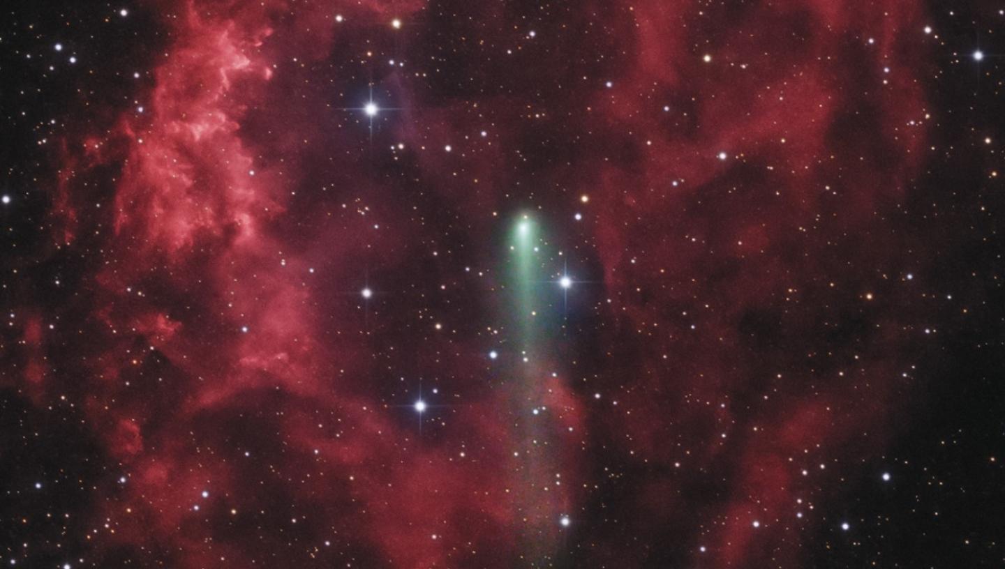 Image of green comet going through a red nebula, which resembles a rose