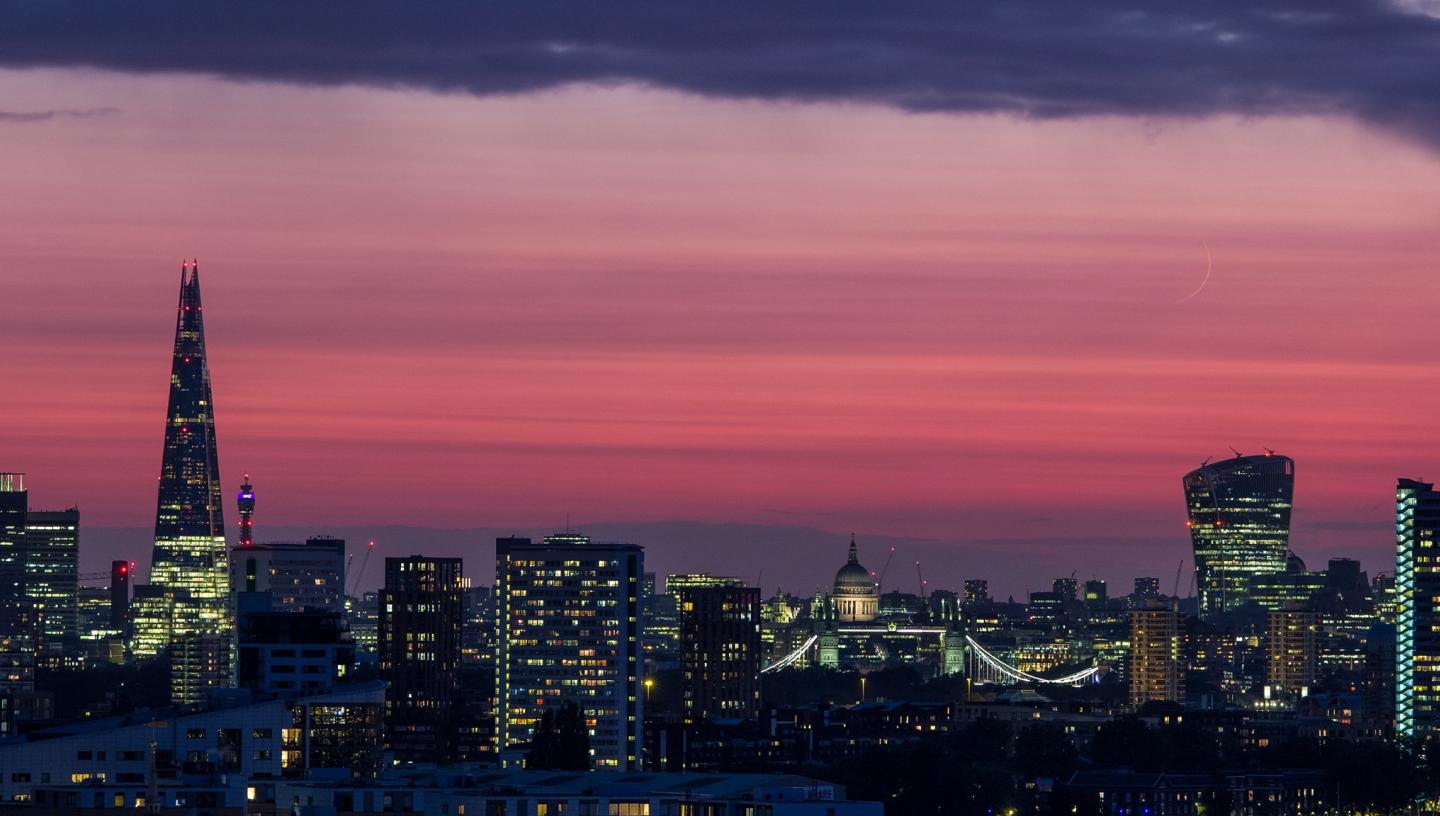 Image of London at dusk with a pink sky and a very thin crescent moon visible