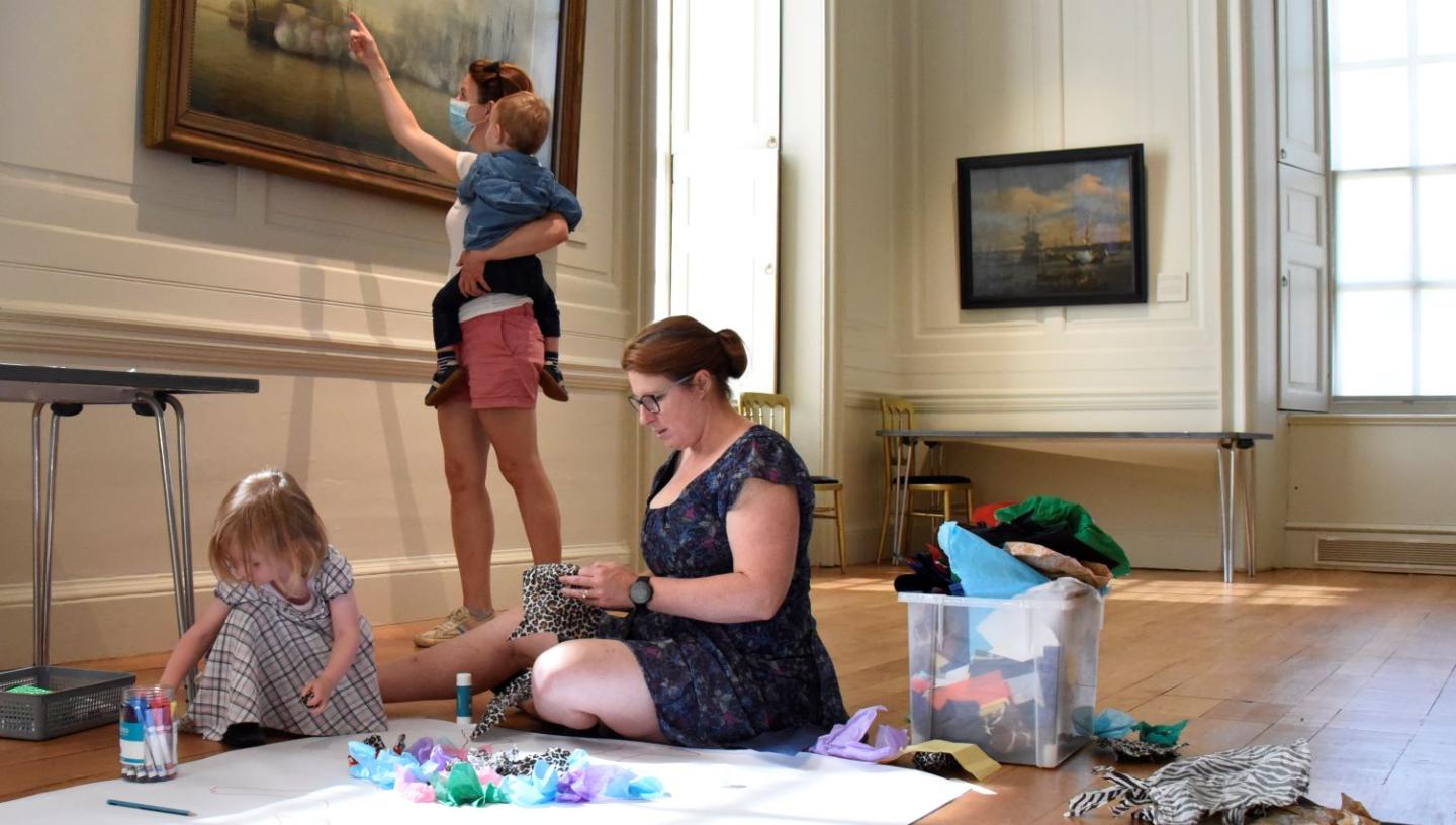 Families create portraits with craft materials on the floor of the Queen's House