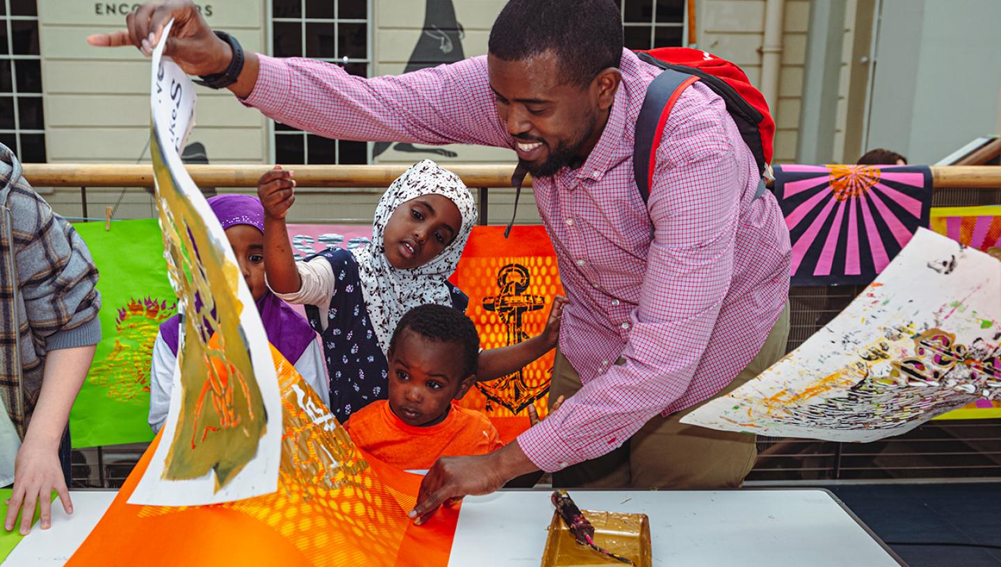 A family takes part in a print workshop during World Oceans Day at the National Maritime Museum. The father is peeling away a sheet of paper as two children look on