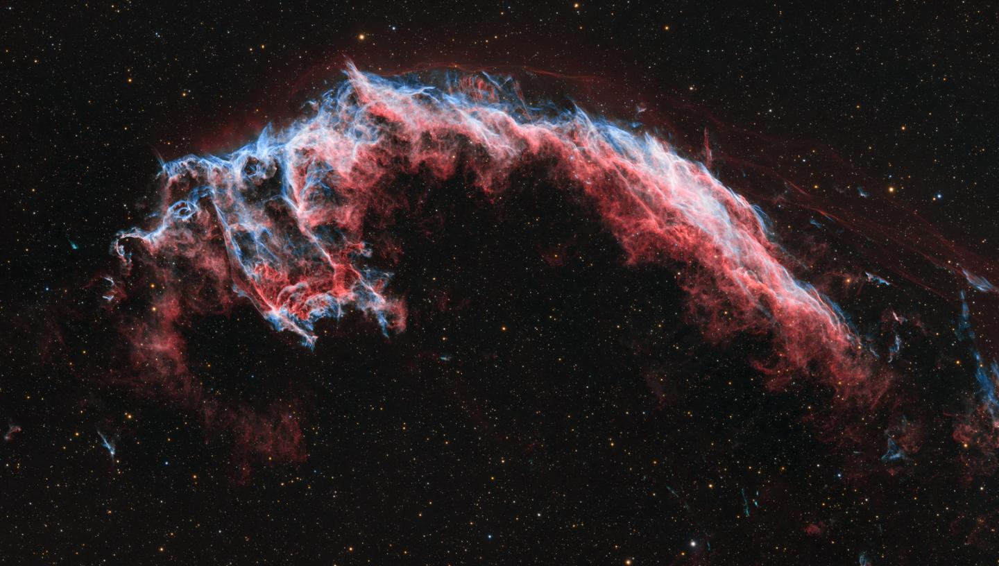 Deep space image showing the Veil Nebula, a glowing cloud of gas apparently floating in the darkness of space