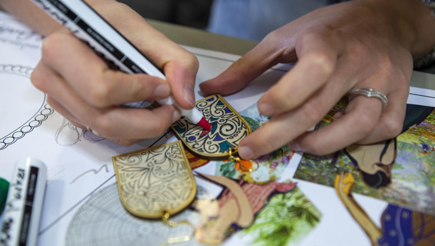 Close-up shot of a person's hands as they use a felt-tip pen to draw an intricate pattern on a small piece of wood