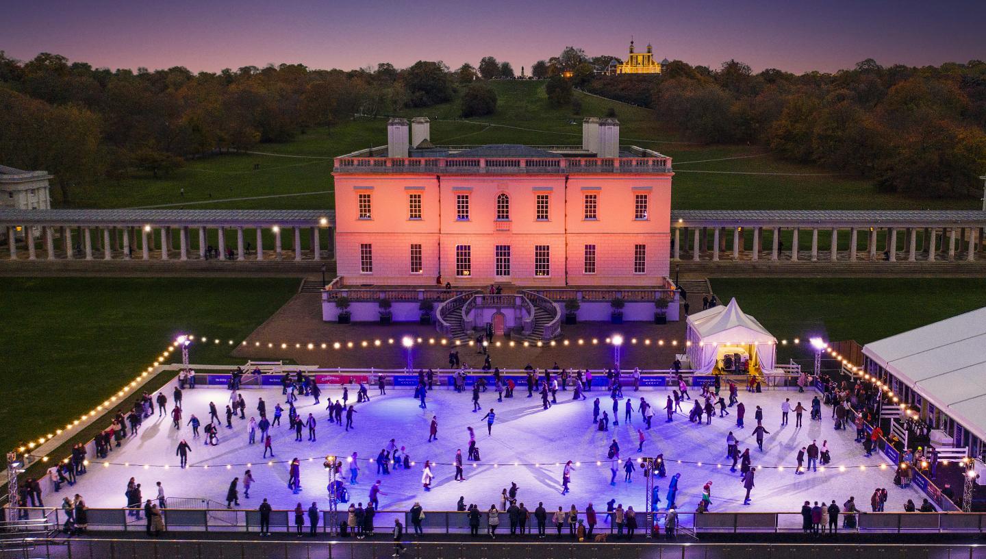 Image of the Queen's House in Greenwich lit in pink lights at dusk, with ice rink in front with lots of people on it, lit up in blue