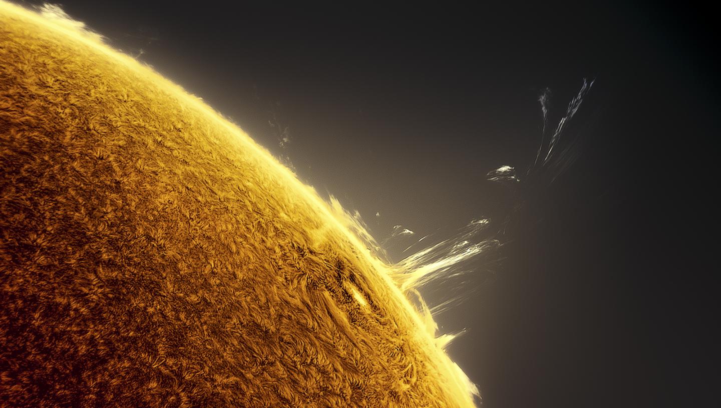 A close-up telescope view of the Sun's surface, with a solar flare bursting out and stretching its trail into the universe