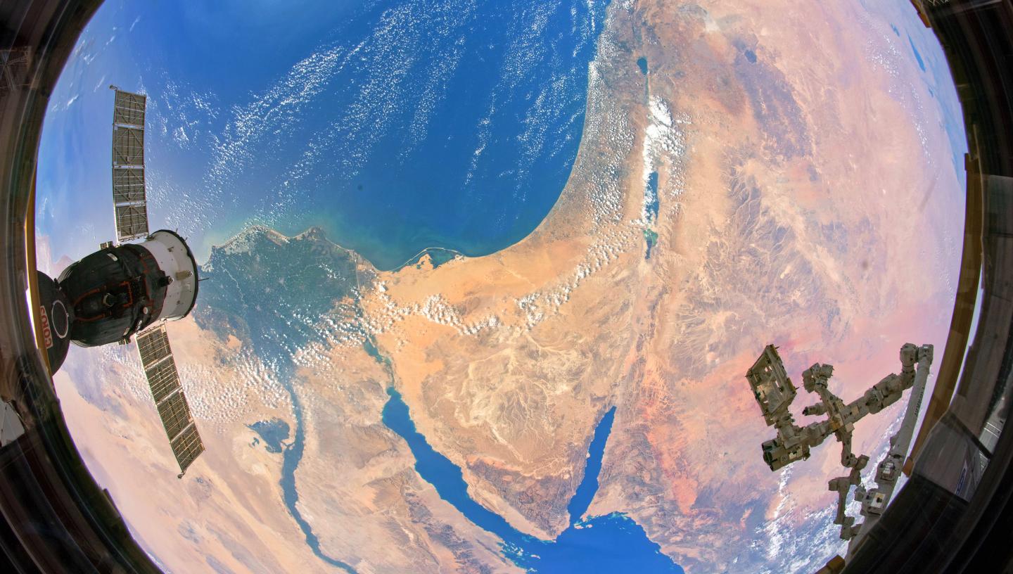 A fish-eye view of Earth taken from a satellite. Yellow and orange desert is visible along with deep blue ocean and wispy clouds
