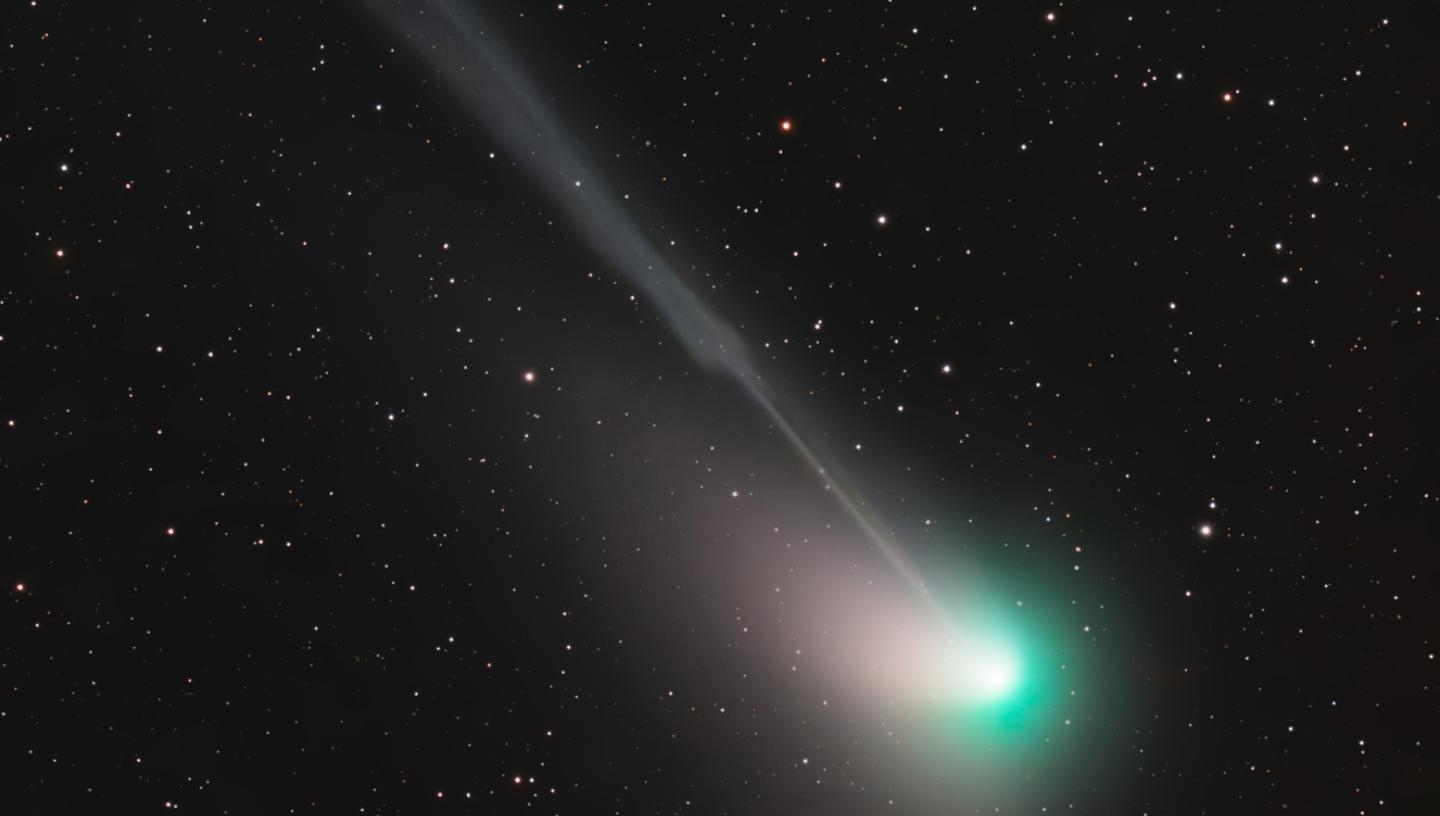 Photograph of a comet taken using a telescope. The comet itself appears as a bright green light, with the tail streaming out diagonally behind