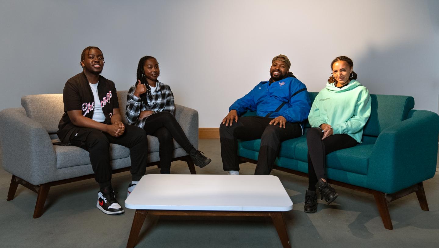 A group of people sit on a sofa in conversation