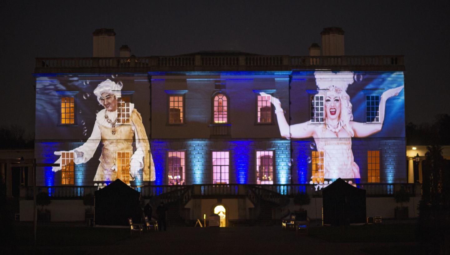 A photo of Adam All and Apple Derrieres in royal attire projected onto the front of the Queen's House as part of the Fierce Queens event to celebrate LGBTQ+ History Month