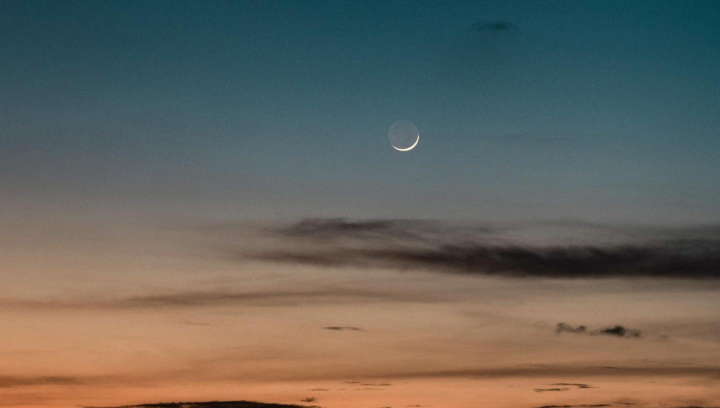 Image of new crescent Moon against the sky with sunset and black clouds