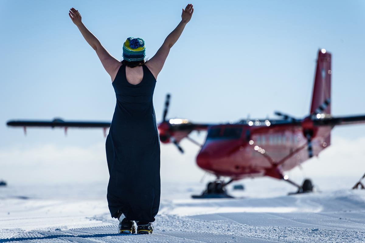 A woman in salopettes looking away from the camera cheers a plane that has just landed on the ice