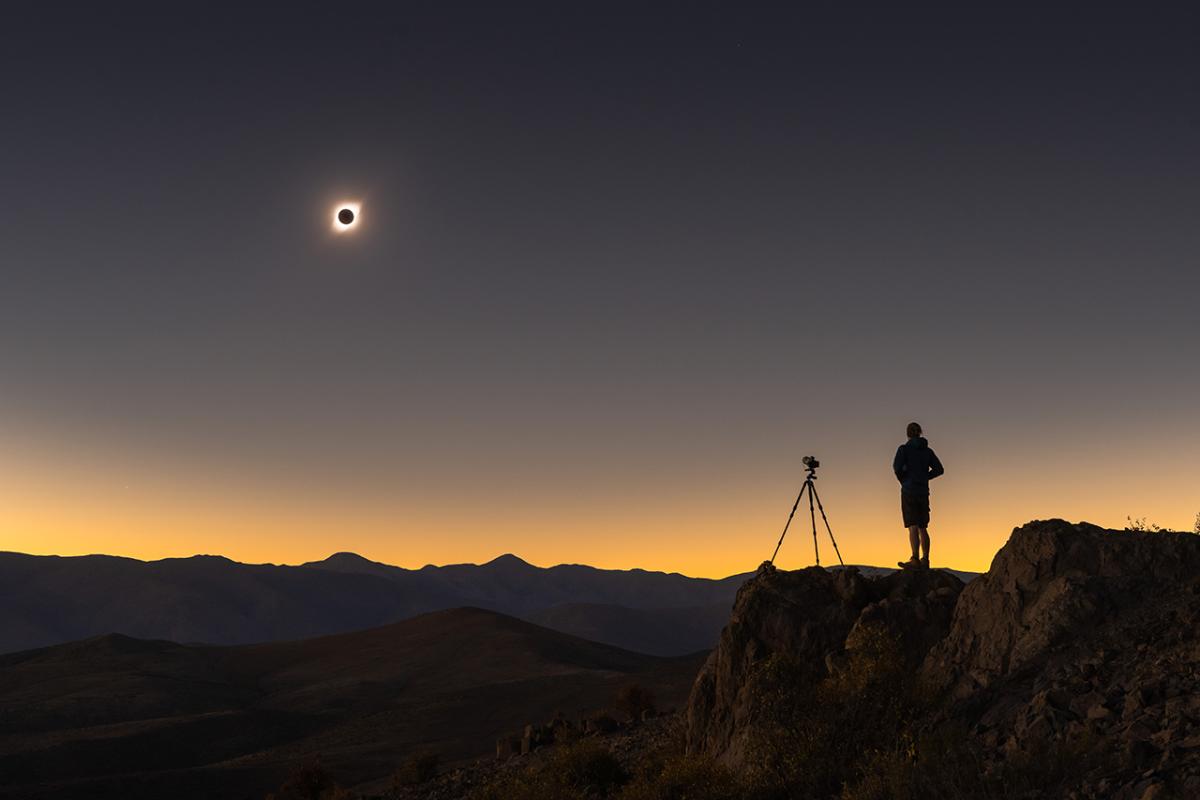 Image of person and a camera on a tripod taking a photo of the solar eclipse