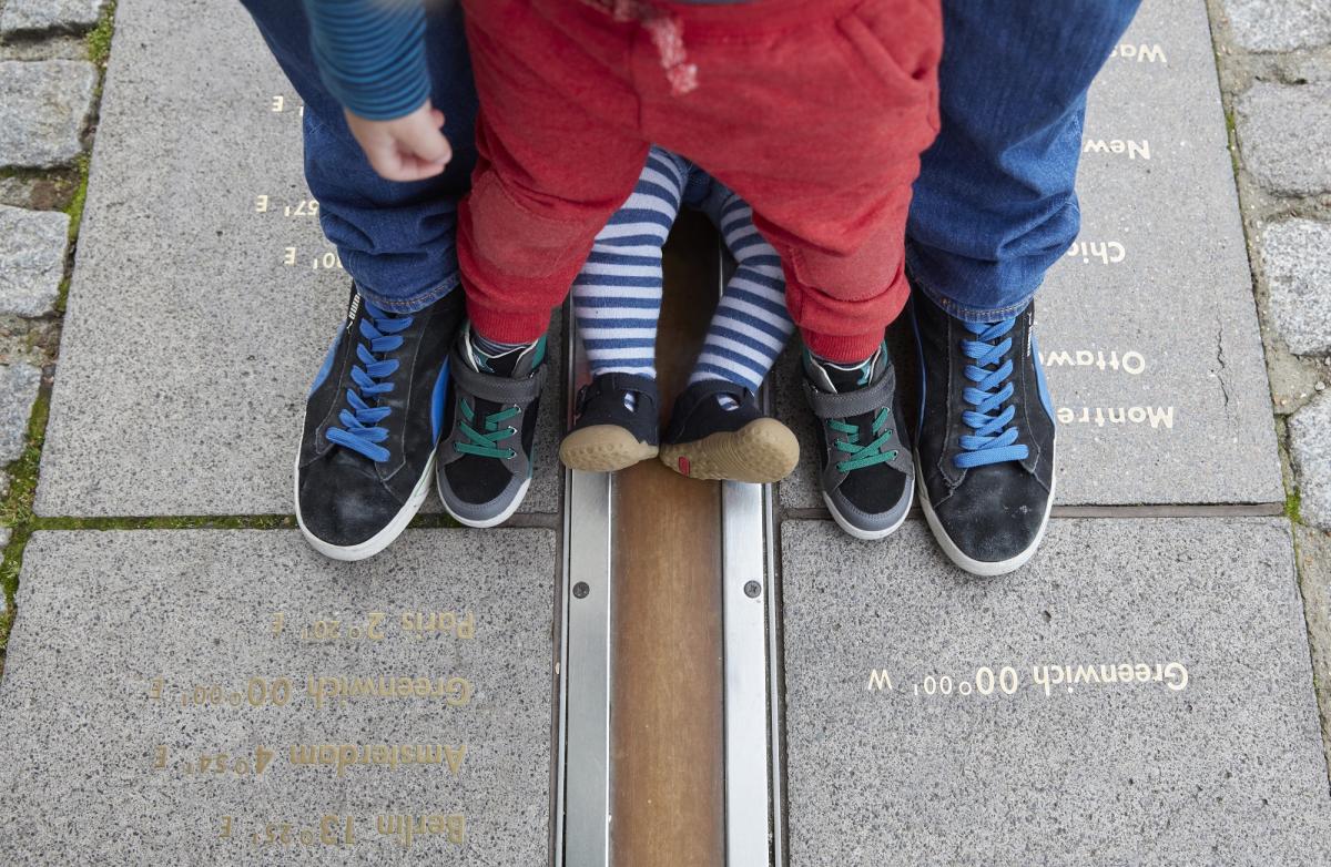 A adult and two children's feet, one foot each side of the meridian line