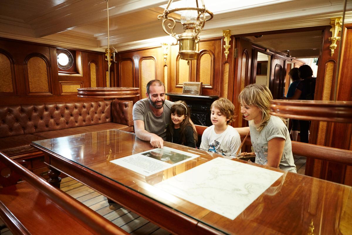 A family sits on leather padded seats inside the wood panelled captain's cabin of Cutty Sark