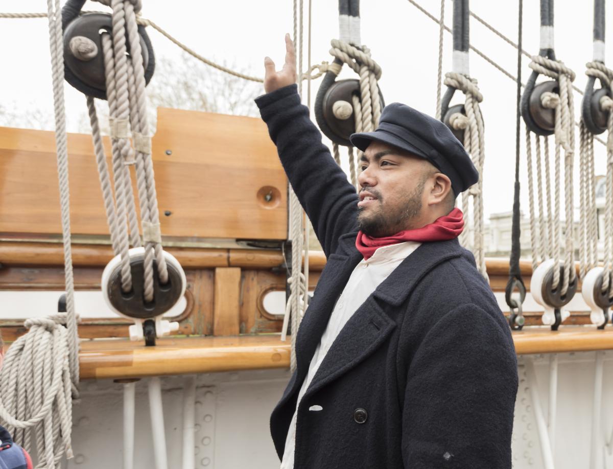 James Robson the cook, one of the characters you can meet on board Cutty Sark. He wears a flat cap and red scarf, and is pointing at the ship's rigging