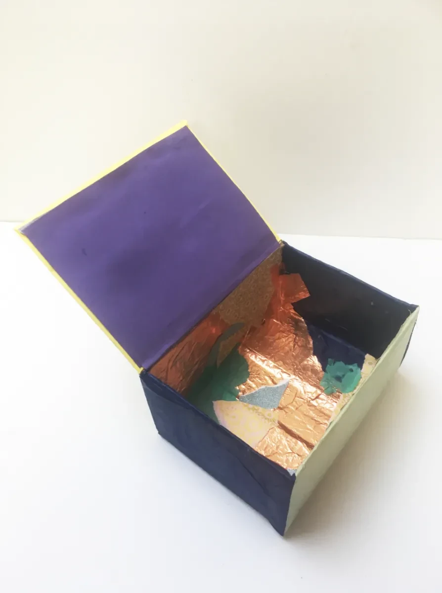 The inside of a decorated cardboard box, with scraps of paper stuck around the interior