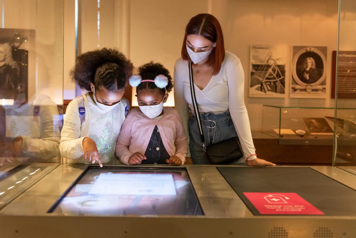 A family looks at an interactive display at the Royal Observatory. They are wearing face masks