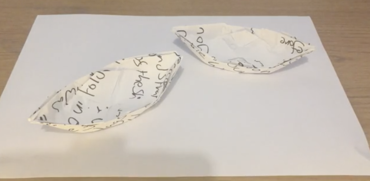 2 ships folded out of paper using origami. There is some illegible writing on the paper.