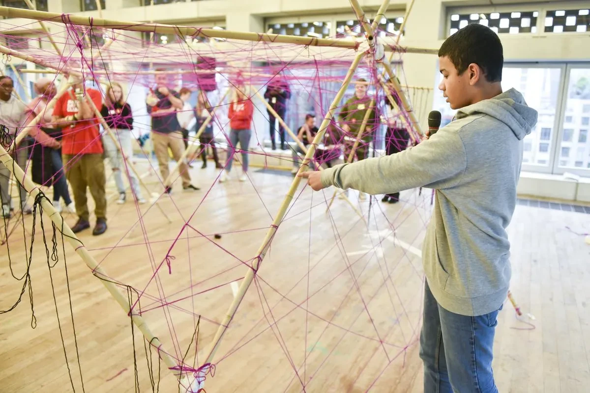a young person is speaking on a mic in front of a sculpture