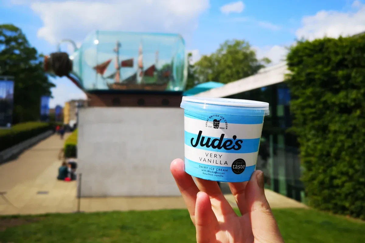A vanilla ice cream tub is held up in front of a 'Ship in a Bottle' sculpture.