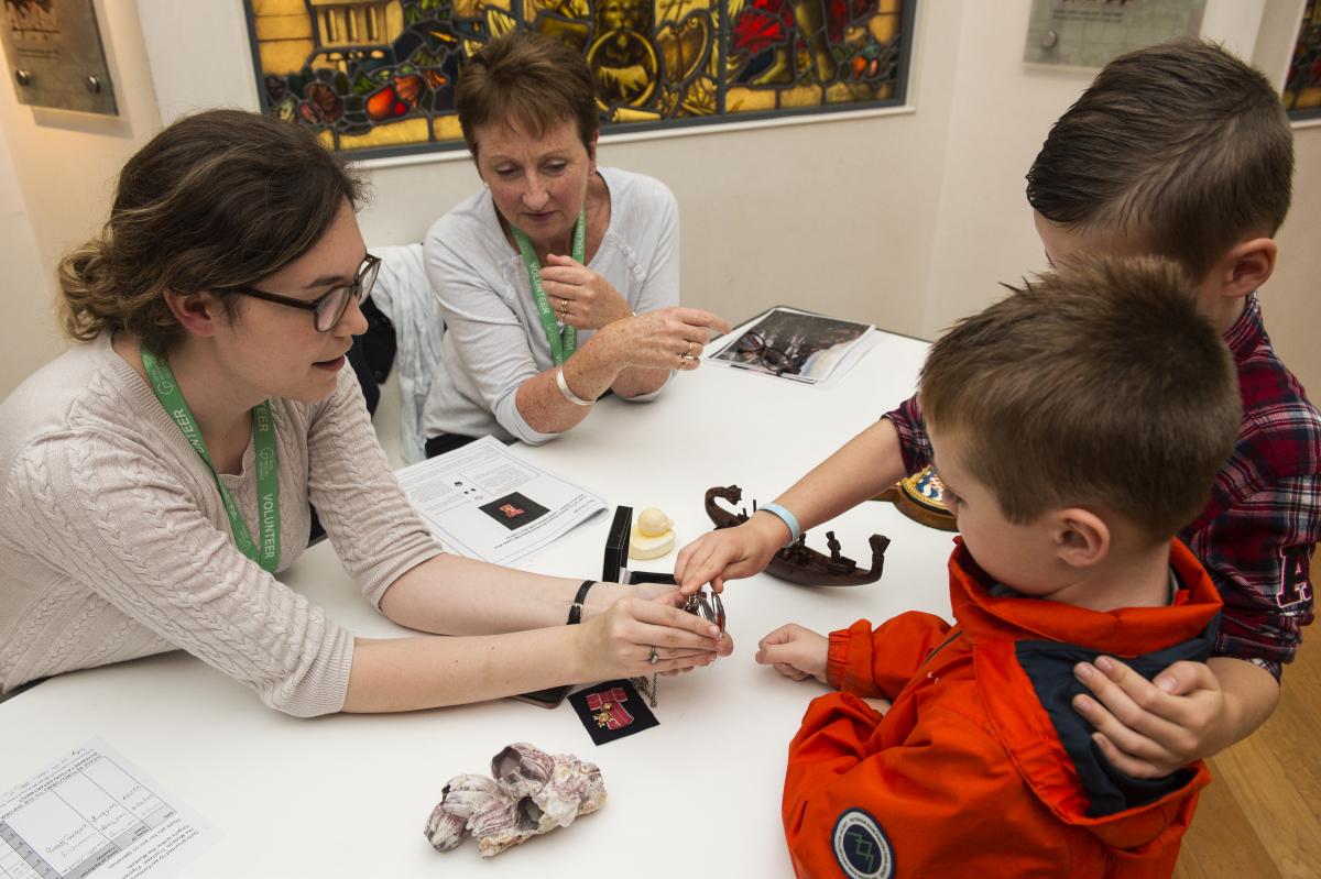 Two adults are showing two children some objects that are laid out on a table. 