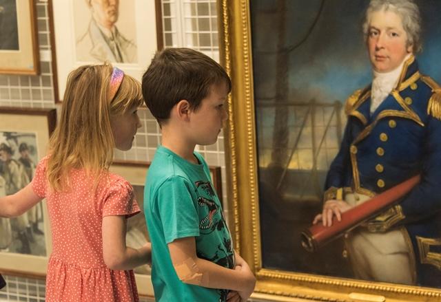 Two children look at a painting of a man in Naval uniform.