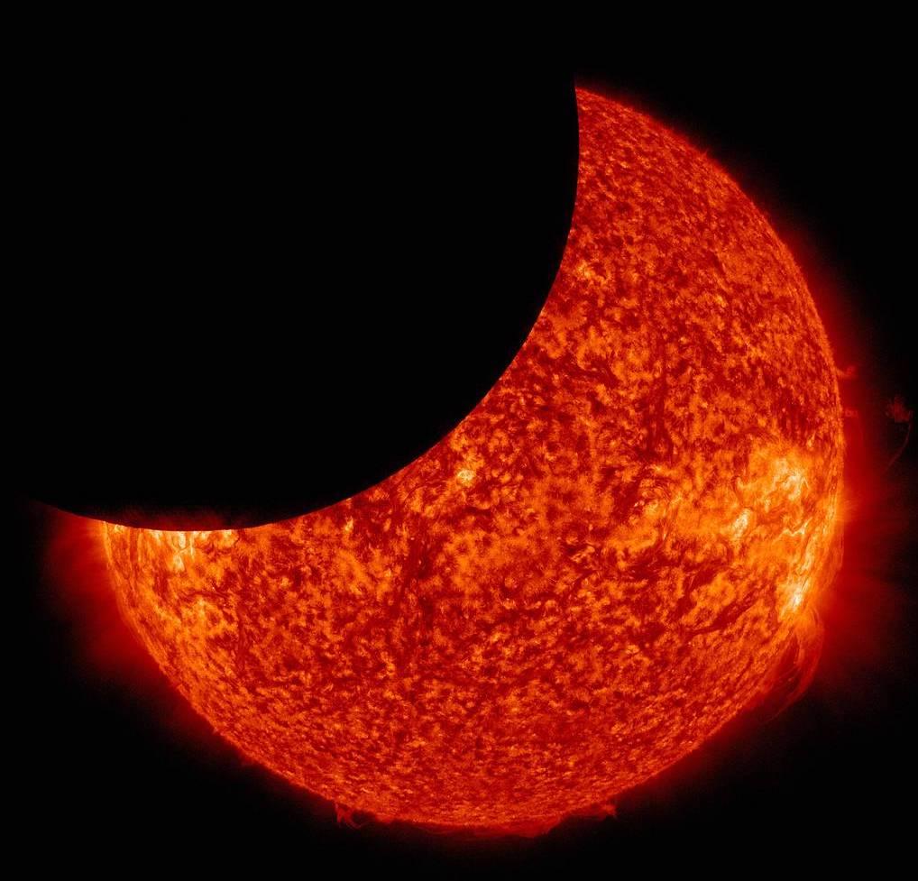 A telescope view of a partial solar eclipse, with the black shadow of the Moon crossing the fiery red disc of the Sun