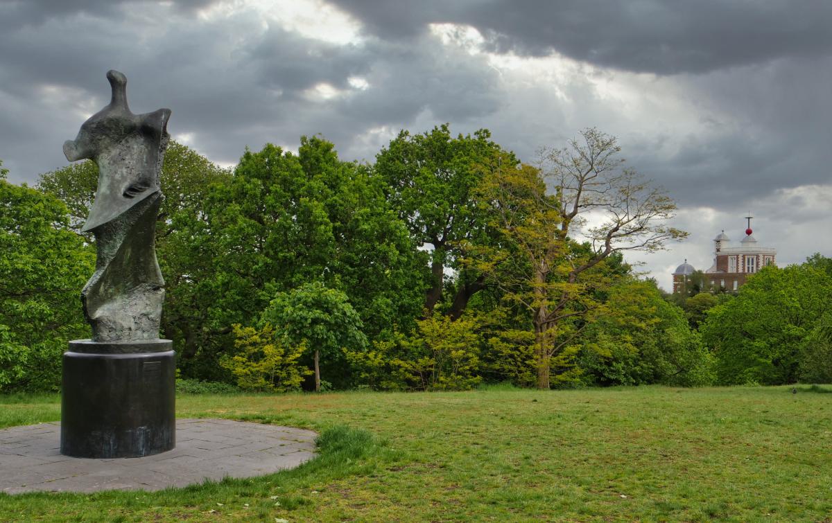 An abstract bronze sculpture in Greenwich Park with the Royal Observatory in the background