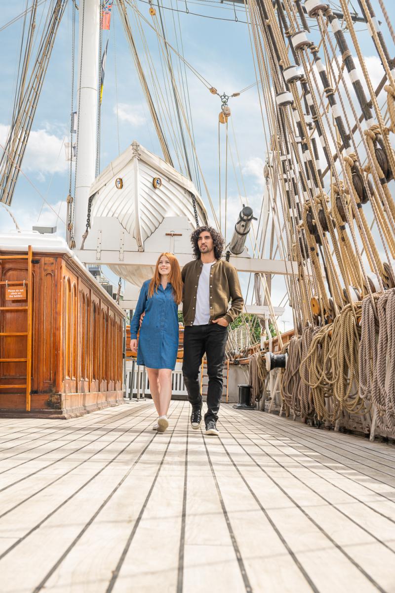 A couple walks along the main deck of historic ship Cutty Sark in summer, with rigging and masts above them